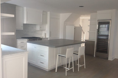 Photo of a mid-sized transitional single-wall eat-in kitchen in New York with shaker cabinets, white cabinets, concrete benchtops, white splashback, marble splashback, panelled appliances, medium hardwood floors, with island, grey floor and a double-bowl sink.