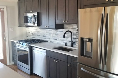 Eat-in kitchen - mid-sized contemporary single-wall dark wood floor and brown floor eat-in kitchen idea in New York with recessed-panel cabinets, dark wood cabinets, an island, an undermount sink, quartzite countertops, multicolored backsplash, marble backsplash, stainless steel appliances and white countertops