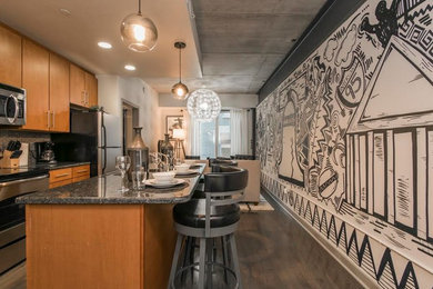 Example of a large minimalist galley medium tone wood floor and gray floor open concept kitchen design in Philadelphia with a drop-in sink, flat-panel cabinets, brown cabinets, granite countertops, stainless steel appliances, an island, beige backsplash and black countertops