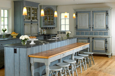 Inspiration for a large timeless galley light wood floor and brown floor eat-in kitchen remodel in Philadelphia with a single-bowl sink, glass-front cabinets, blue cabinets, limestone countertops, white backsplash, stainless steel appliances and an island