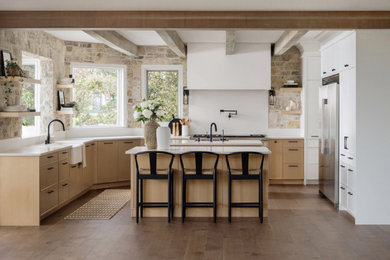 Example of a large transitional u-shaped medium tone wood floor, brown floor and exposed beam eat-in kitchen design in Calgary with a farmhouse sink, shaker cabinets, light wood cabinets, quartz countertops, multicolored backsplash, stone slab backsplash, stainless steel appliances, two islands and white countertops