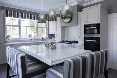 Mid-sized traditional u-shaped separate kitchen in Kent with shaker cabinets, white cabinets, quartzite benchtops, black appliances, with island, white benchtop, a double-bowl sink, grey floor and white splashback.