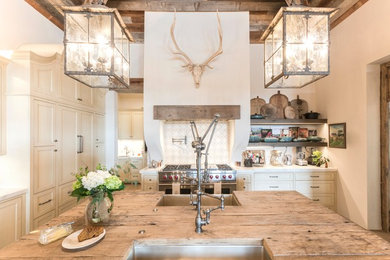 Huge farmhouse medium tone wood floor and brown floor eat-in kitchen photo in Austin with a farmhouse sink, shaker cabinets, beige cabinets, wood countertops, brown countertops, white backsplash, terra-cotta backsplash, paneled appliances and an island