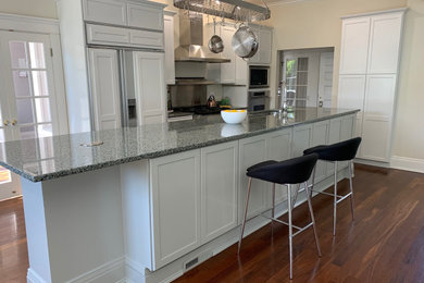 Example of a large transitional single-wall dark wood floor and brown floor enclosed kitchen design in Seattle with an undermount sink, shaker cabinets, white cabinets, granite countertops, gray backsplash, metal backsplash, stainless steel appliances, an island and gray countertops