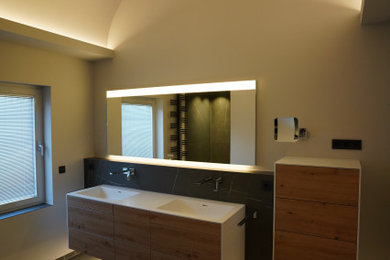 Inredning av ett modernt mycket stort vit vitt badrum med dusch, med släta luckor, skåp i ljust trä, en dusch i en alkov, en vägghängd toalettstol, svart och vit kakel, marmorkakel, grå väggar, marmorgolv, ett väggmonterat handfat, bänkskiva i akrylsten, svart golv och med dusch som är öppen