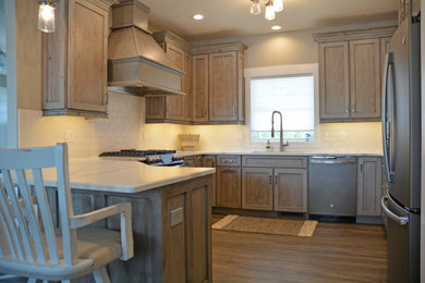 Photo of a small traditional u-shaped kitchen/diner in Other with a submerged sink, recessed-panel cabinets, medium wood cabinets, engineered stone countertops, white splashback, metro tiled splashback, stainless steel appliances, a breakfast bar, brown floors and white worktops.