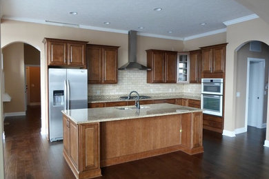 Example of a large classic l-shaped dark wood floor and brown floor open concept kitchen design in Indianapolis with an undermount sink, raised-panel cabinets, dark wood cabinets, granite countertops, stainless steel appliances, beige backsplash, stone tile backsplash and an island