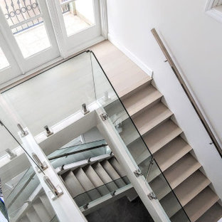 Immagine di una grande scala minimalista con pedata in legno, alzata in vetro e parapetto in metallo