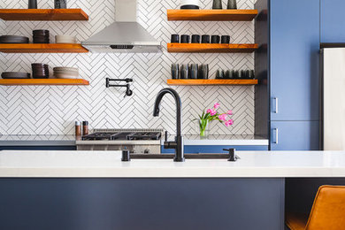 Example of a trendy galley medium tone wood floor and brown floor kitchen design in San Francisco with flat-panel cabinets, blue cabinets, white backsplash, mosaic tile backsplash, stainless steel appliances, an island and white countertops