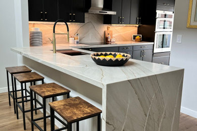 Inspiration for a mid-sized coastal laminate floor, brown floor and vaulted ceiling eat-in kitchen remodel in San Diego with flat-panel cabinets, black cabinets, quartzite countertops, gray backsplash, granite backsplash, stainless steel appliances and gray countertops