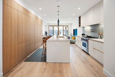 Modern inredning av ett mellanstort vit vitt kök, med en undermonterad diskho, släta luckor, vita skåp, bänkskiva i kvartsit, grönt stänkskydd, stänkskydd i porslinskakel, ljust trägolv, en köksö och flerfärgat golv