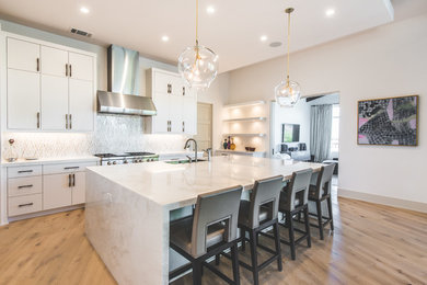 Large trendy l-shaped light wood floor and beige floor open concept kitchen photo in Austin with an undermount sink, flat-panel cabinets, white cabinets, marble countertops, white backsplash, porcelain backsplash, stainless steel appliances and an island