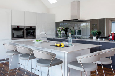 Large contemporary l-shaped open plan kitchen in Other with an undermount sink, flat-panel cabinets, grey cabinets, quartzite benchtops, grey splashback, glass sheet splashback, stainless steel appliances, dark hardwood floors, with island and brown floor.