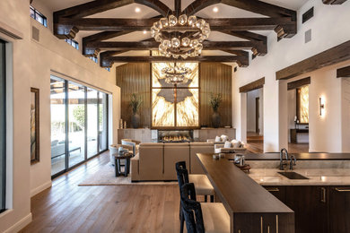 Example of a large southwest open concept medium tone wood floor, brown floor and exposed beam living room design in Phoenix with a bar, white walls, a standard fireplace, a stone fireplace and a concealed tv