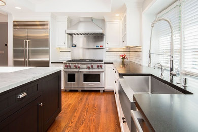 Example of a large transitional l-shaped medium tone wood floor and brown floor enclosed kitchen design in San Francisco with a farmhouse sink, glass-front cabinets, white cabinets, white backsplash, subway tile backsplash, stainless steel appliances and an island