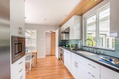Minimalist galley medium tone wood floor enclosed kitchen photo in San Francisco with an undermount sink, flat-panel cabinets, white cabinets, glass tile backsplash, stainless steel appliances and no island