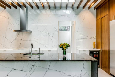 Bild på ett stort funkis grå grått kök, med en undermonterad diskho, släta luckor, skåp i mellenmörkt trä, marmorbänkskiva, vitt stänkskydd, stänkskydd i porslinskakel, rostfria vitvaror, klinkergolv i porslin, en köksö och beiget golv