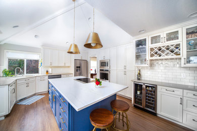Vaulted ceiling kitchen photo in Portland with an undermount sink, white cabinets, quartz countertops, subway tile backsplash, stainless steel appliances, an island and shaker cabinets