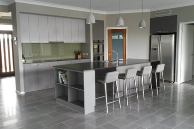 Inspiration for a mid-sized galley kitchen in Brisbane with a double-bowl sink, grey cabinets, green splashback, glass sheet splashback, stainless steel appliances, porcelain floors and with island.