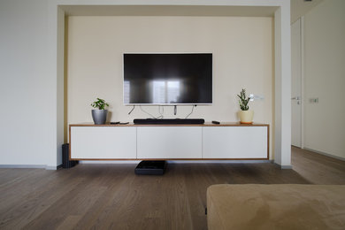 Пример оригинального дизайна: открытая гостиная комната в современном стиле с белыми стенами, паркетным полом среднего тона и телевизором на стене