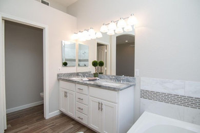 Inspiration for a large transitional master beige tile and ceramic tile medium tone wood floor and brown floor alcove bathtub remodel in Phoenix with shaker cabinets, white cabinets, gray walls, an undermount sink and quartzite countertops