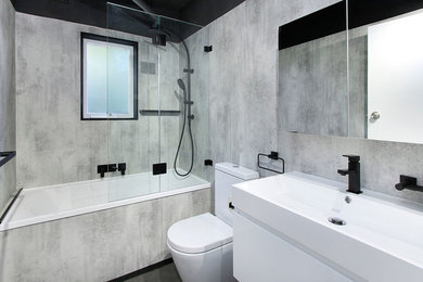Inspiration for a mid-sized industrial master bathroom in Wollongong with flat-panel cabinets, white cabinets, a drop-in tub, a shower/bathtub combo, a one-piece toilet, grey walls, vinyl floors, grey floor and a hinged shower door.