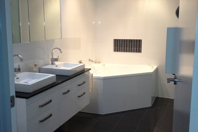 Mid-sized contemporary master bathroom in Brisbane with an undermount sink, flat-panel cabinets, white cabinets, glass benchtops, a drop-in tub, a corner shower, a two-piece toilet, white tile, ceramic tile, white walls and porcelain floors.