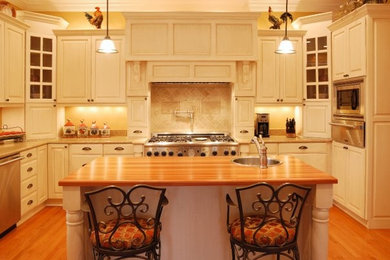 Eat-in kitchen - mid-sized farmhouse u-shaped light wood floor eat-in kitchen idea in Other with a single-bowl sink, raised-panel cabinets, white cabinets, wood countertops, beige backsplash, ceramic backsplash, stainless steel appliances and an island