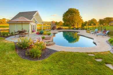 Design ideas for a large transitional backyard custom-shaped pool in Other with a pool house and concrete pavers.