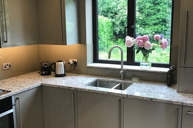 Photo of a medium sized contemporary l-shaped enclosed kitchen in Hertfordshire with a built-in sink, flat-panel cabinets, quartz worktops, glass sheet splashback, black appliances, porcelain flooring, no island, grey floors and multicoloured worktops.