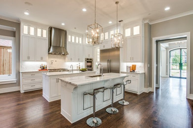 Inspiration for a large transitional l-shaped dark wood floor and brown floor enclosed kitchen remodel in Dallas with an undermount sink, recessed-panel cabinets, white cabinets, marble countertops, white backsplash, marble backsplash, stainless steel appliances, two islands and white countertops