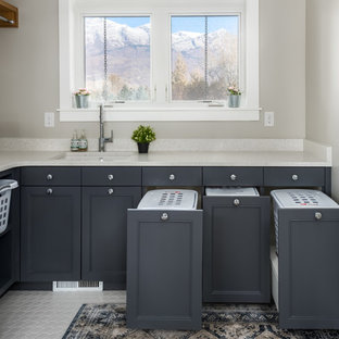 Ejemplo de cuarto de lavado en L, tradicional renovado, con fregadero bajoencimera, armarios con paneles empotrados, puertas de armario grises, paredes grises, suelo blanco y encimeras beige