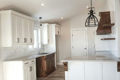 Example of a mid-sized mountain style galley medium tone wood floor and brown floor open concept kitchen design in Calgary with an undermount sink, recessed-panel cabinets, white cabinets, marble countertops, white backsplash, ceramic backsplash and a peninsula
