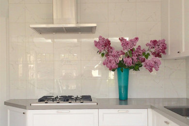 This is an example of a mid-sized transitional l-shaped separate kitchen with recessed-panel cabinets, white cabinets, quartz benchtops, white splashback, stone tile splashback, no island and grey benchtop.