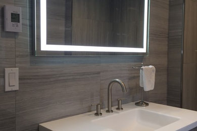 Mid-sized minimalist 3/4 gray tile and porcelain tile limestone floor and beige floor bathroom photo in Burlington with flat-panel cabinets, gray cabinets, a one-piece toilet, gray walls, an integrated sink and solid surface countertops