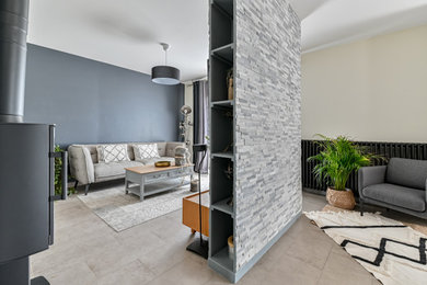 Cette photo montre une grande salle de séjour tendance ouverte avec un mur bleu, un sol en carrelage de céramique, un poêle à bois, un téléviseur fixé au mur et un sol gris.