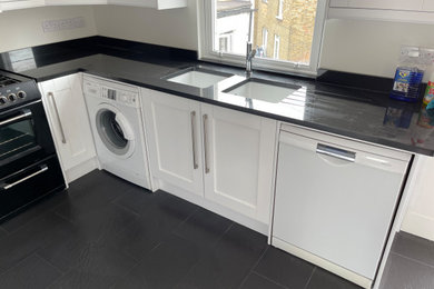 Example of a minimalist u-shaped eat-in kitchen design in London with a double-bowl sink, white cabinets, granite countertops, white appliances, an island and black countertops