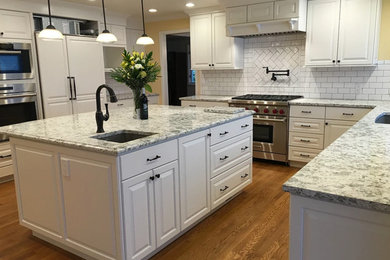 Enclosed kitchen - mid-sized transitional u-shaped medium tone wood floor and brown floor enclosed kitchen idea in Seattle with an undermount sink, raised-panel cabinets, white cabinets, granite countertops, white backsplash, subway tile backsplash, paneled appliances, an island and multicolored countertops
