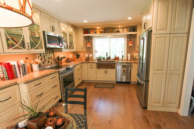 Photo of a mid-sized transitional l-shaped eat-in kitchen in San Francisco with a farmhouse sink, raised-panel cabinets, white cabinets, granite benchtops, beige splashback, mosaic tile splashback, stainless steel appliances, medium hardwood floors, no island, brown floor and beige benchtop.