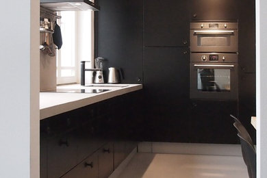 Mid-sized trendy l-shaped concrete floor eat-in kitchen photo in Amsterdam with a drop-in sink, flat-panel cabinets, black cabinets, concrete countertops, gray backsplash and black appliances