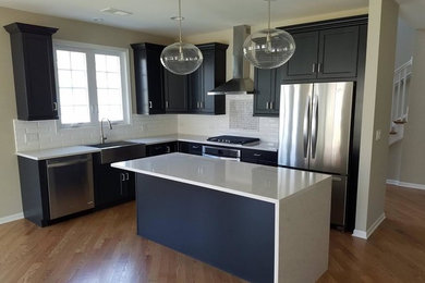 Inspiration for a large transitional l-shaped light wood floor and brown floor enclosed kitchen remodel in Chicago with a farmhouse sink, shaker cabinets, dark wood cabinets, solid surface countertops, white backsplash, subway tile backsplash, stainless steel appliances and an island