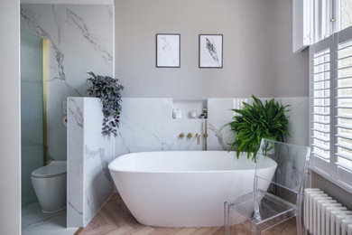 This is an example of a medium sized contemporary grey and white ensuite bathroom in London with flat-panel cabinets, a freestanding bath, a walk-in shower, a one-piece toilet, beige walls, wood-effect flooring, marble worktops, beige floors, a feature wall, double sinks and a floating vanity unit.
