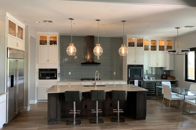 This is an example of a large transitional l-shaped eat-in kitchen in Phoenix with a farmhouse sink, recessed-panel cabinets, dark wood cabinets, quartzite benchtops, blue splashback, glass tile splashback, black appliances, porcelain floors, with island, multi-coloured floor and multi-coloured benchtop.