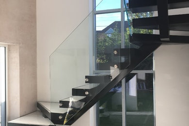 Modern tiled u-shaped glass railing staircase in Essex with open risers.