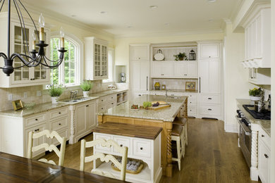 Large elegant u-shaped medium tone wood floor eat-in kitchen photo in Nashville with a drop-in sink, recessed-panel cabinets, white cabinets, granite countertops, beige backsplash, stone tile backsplash, stainless steel appliances and an island