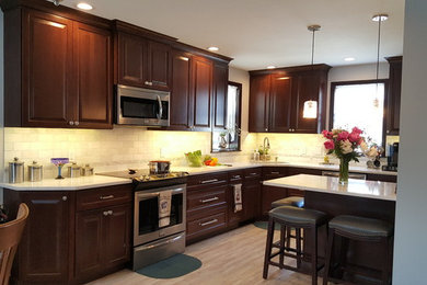 Large transitional l-shaped gray floor and medium tone wood floor eat-in kitchen photo in Philadelphia with an undermount sink, raised-panel cabinets, medium tone wood cabinets, quartz countertops, white backsplash, marble backsplash, stainless steel appliances and an island