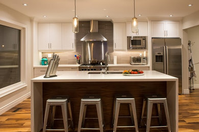Example of a mid-sized transitional single-wall medium tone wood floor eat-in kitchen design in Toronto with an undermount sink, shaker cabinets, white cabinets, quartz countertops, beige backsplash, glass tile backsplash, stainless steel appliances and an island
