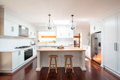 This is an example of a mid-sized industrial u-shaped eat-in kitchen in Perth with an undermount sink, shaker cabinets, white cabinets, quartz benchtops, white splashback, subway tile splashback, stainless steel appliances, dark hardwood floors, with island and white benchtop.