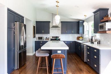 Inspiration for a transitional l-shaped eat-in kitchen in Boston with an undermount sink, shaker cabinets, blue cabinets, quartz benchtops, blue splashback, glass tile splashback, stainless steel appliances, dark hardwood floors, with island, brown floor and white benchtop.