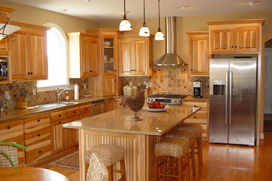 Inspiration for a large timeless l-shaped medium tone wood floor eat-in kitchen remodel in DC Metro with an undermount sink, raised-panel cabinets, light wood cabinets, granite countertops, beige backsplash, stone tile backsplash, stainless steel appliances and an island